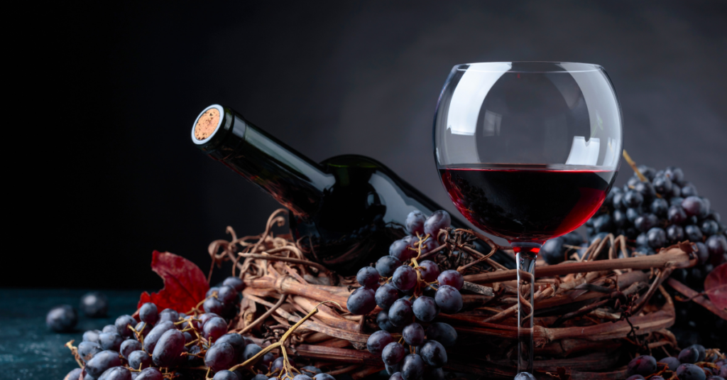 Bottling your wine blog for PBS - red wine in a glass with red grapes and a bottle on top of the grapes and wicker basket